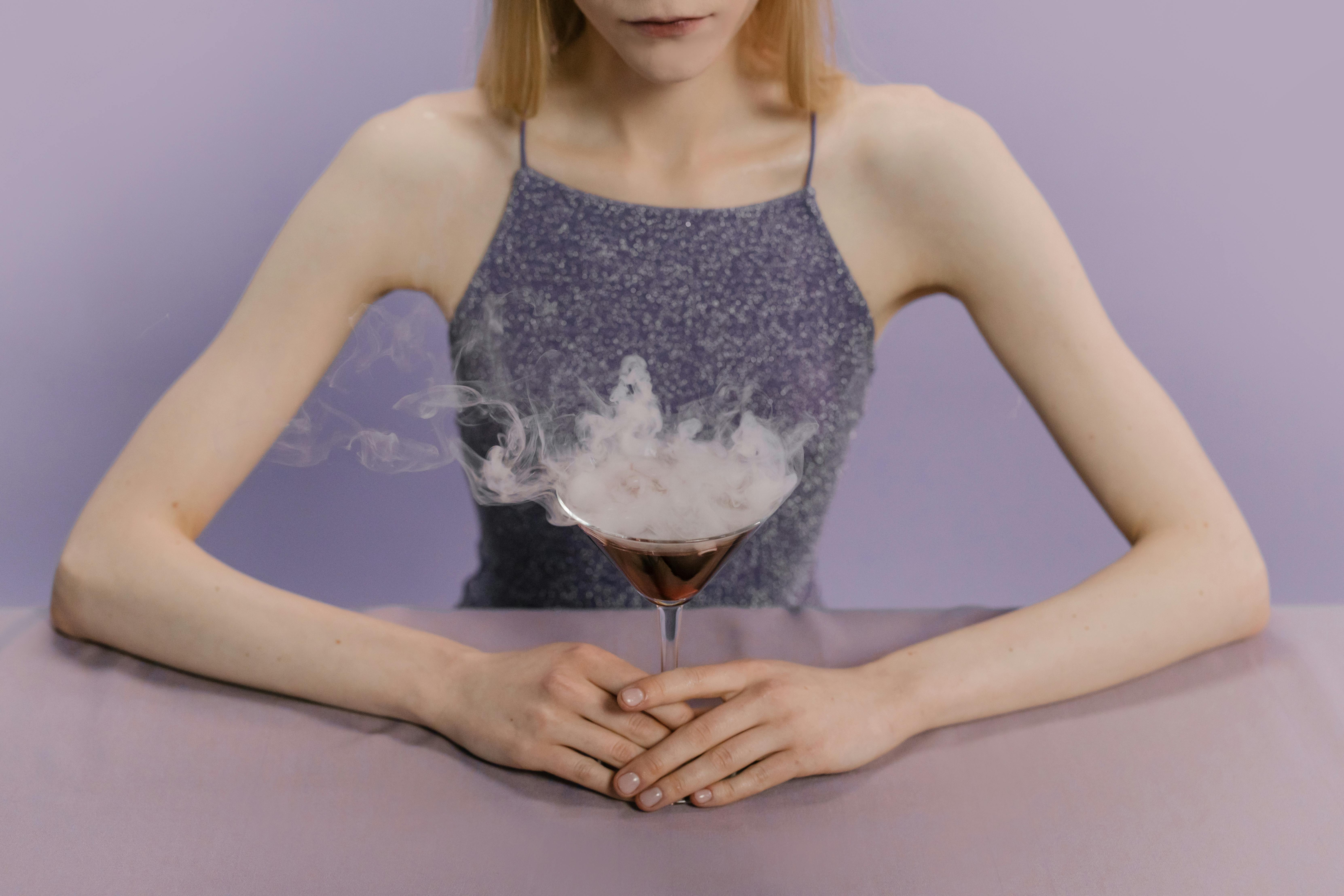 一名女子优雅地坐着，在紫色背景前喝着烟熏马提尼，散发着神秘和魅力