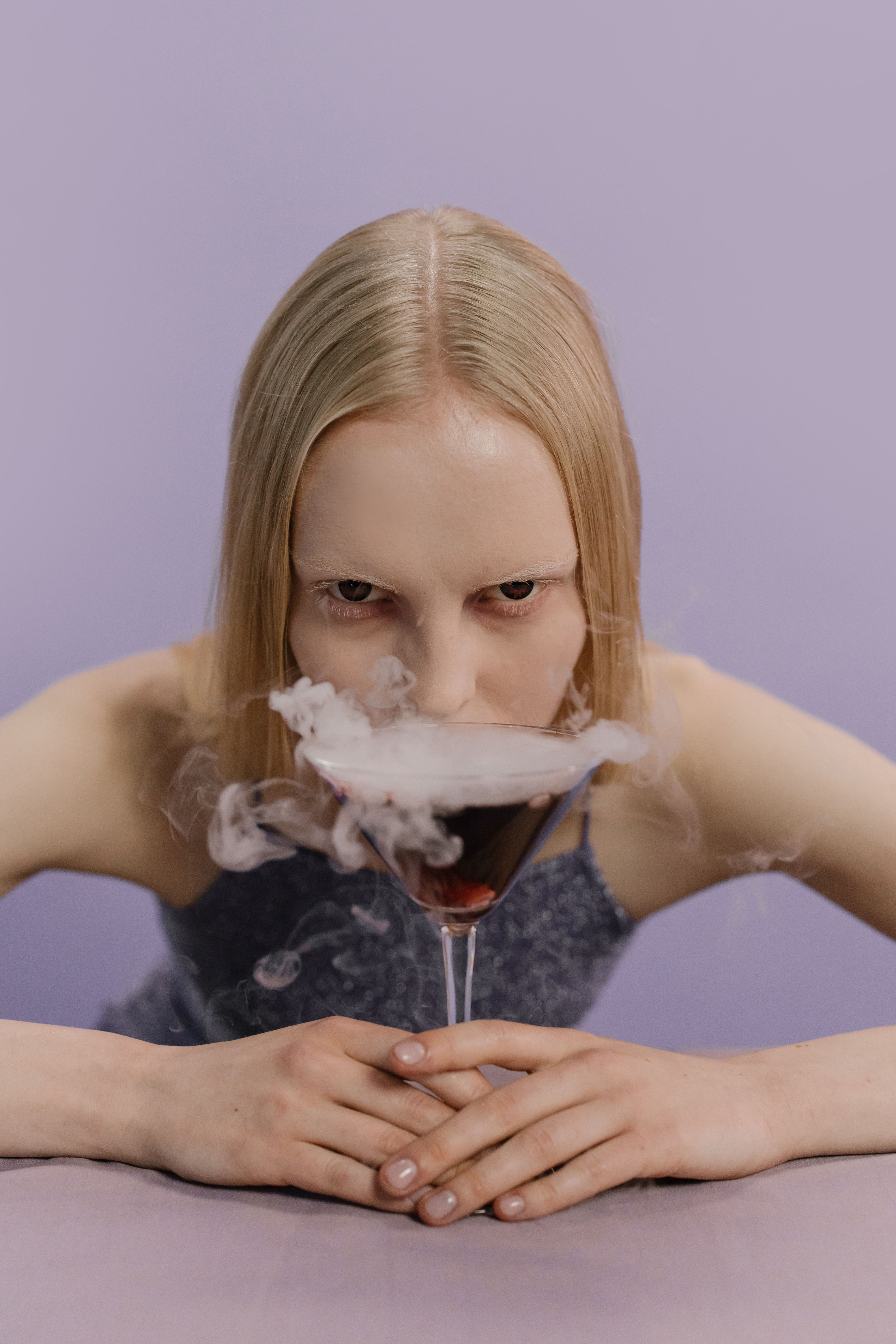 一名女子凝视着紫色背景上的一杯烟熏鸡尾酒