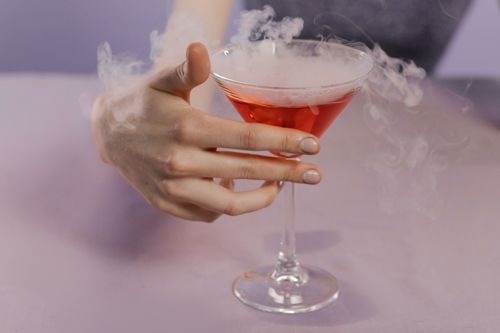 Free Close-up of a hand holding a smoking red cocktail in a glass, capturing elegance and intrigue. Stock Photo