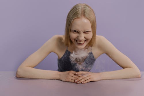 A woman in a spooky Halloween setting smiles menacingly with a dry ice cocktail.