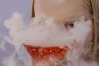 在一个神秘的场景里，一个女人手中的鸡尾酒杯升起烟雾，营造出怪异的万圣节氛围