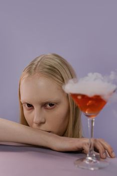 一位神秘女子在紫色背景下摆出拿着吸烟鸡尾酒的姿势，非常适合万圣节主题
