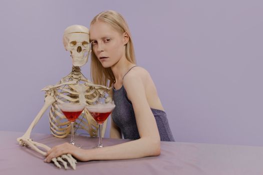 一个女人抱着骷髅坐在柔和的背景下，两人都拿着马提尼酒