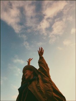 一名女子穿着休闲装，在明亮的蓝天下快乐地伸展双臂