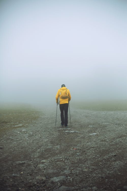 Free Person in Yellow Hoodie Walking on a Rocky Road with Ski Poles on a Foggy Day Stock Photo