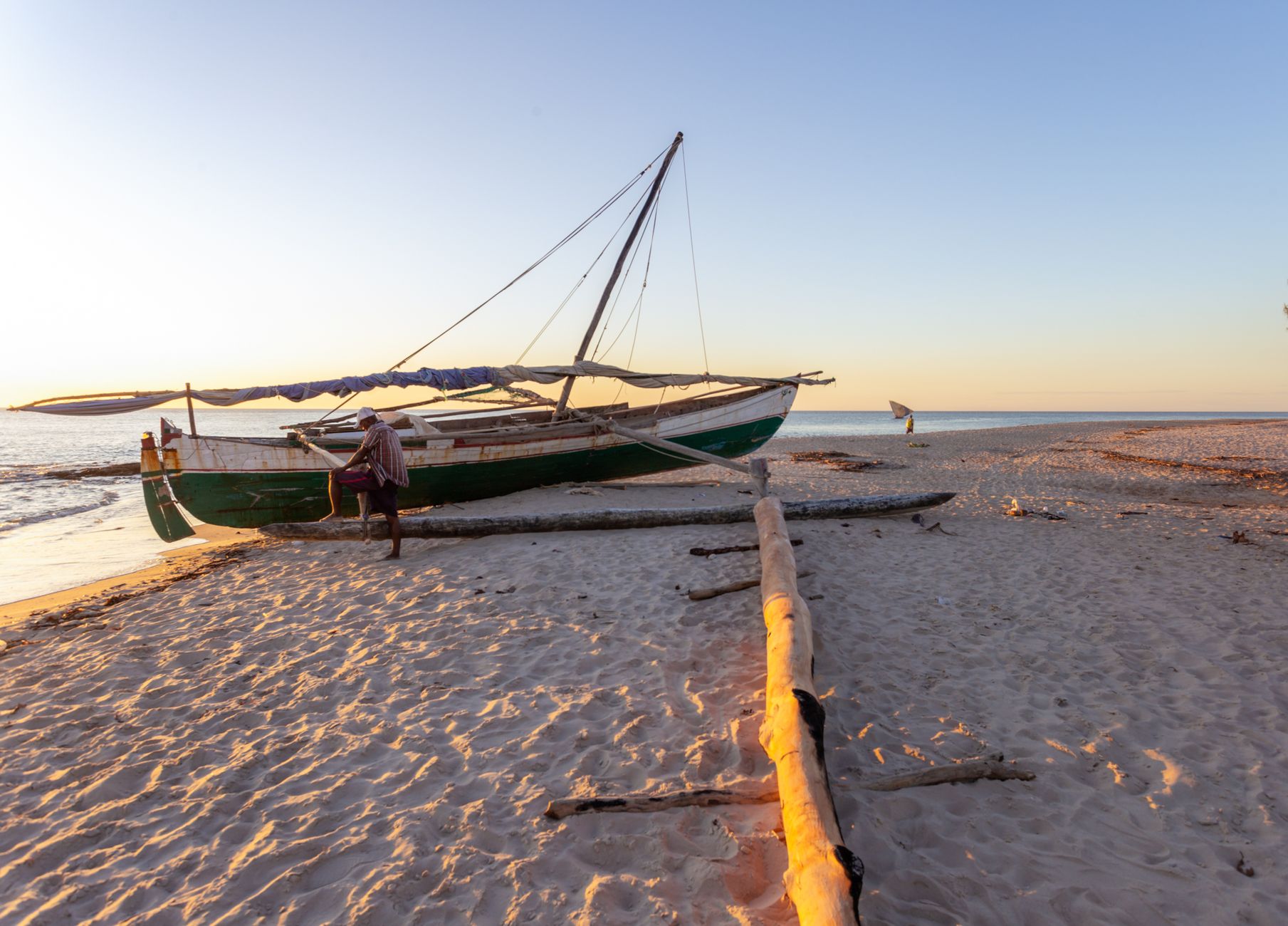 A serene beach scene in Madagascar with a traditional fishing boat during sunset on the sandy shore.