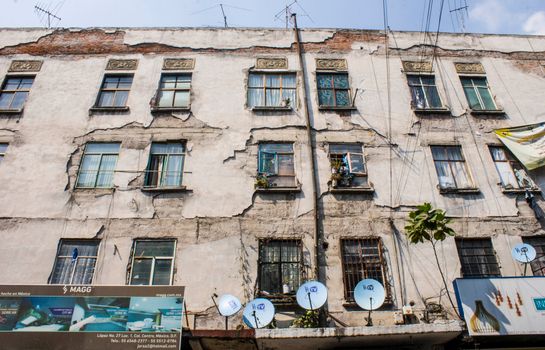 A worn and damaged building facade in Mexico City with satellite dishes and peeling walls.