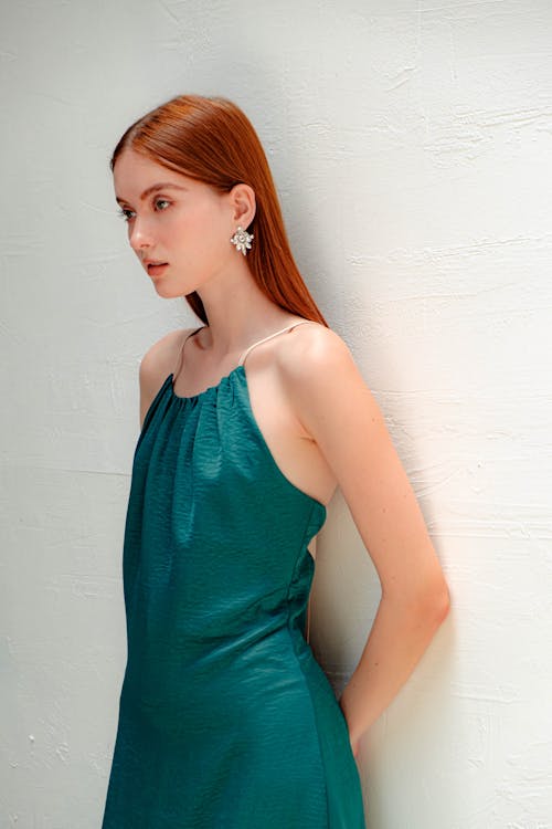 Woman in Green Spaghetti Strap Dress Leaning on a Wall while Looking Afar