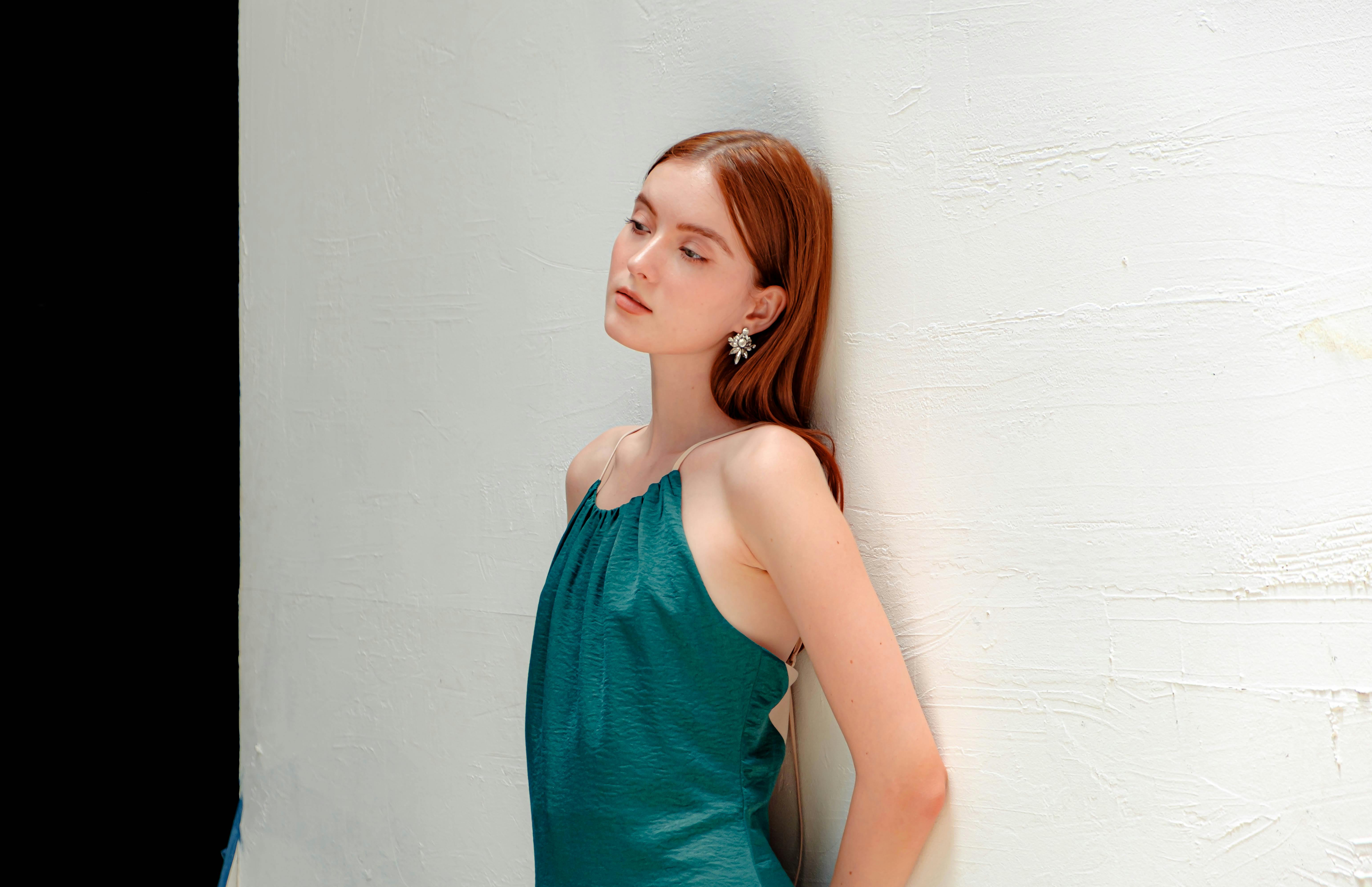 Fashionable woman posing in a green dress, showcasing elegance and style in a studio setting.