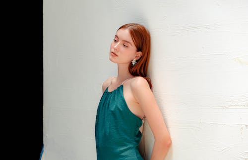 Woman in Blue Sleeveless Dress Leaning on White Wall 
