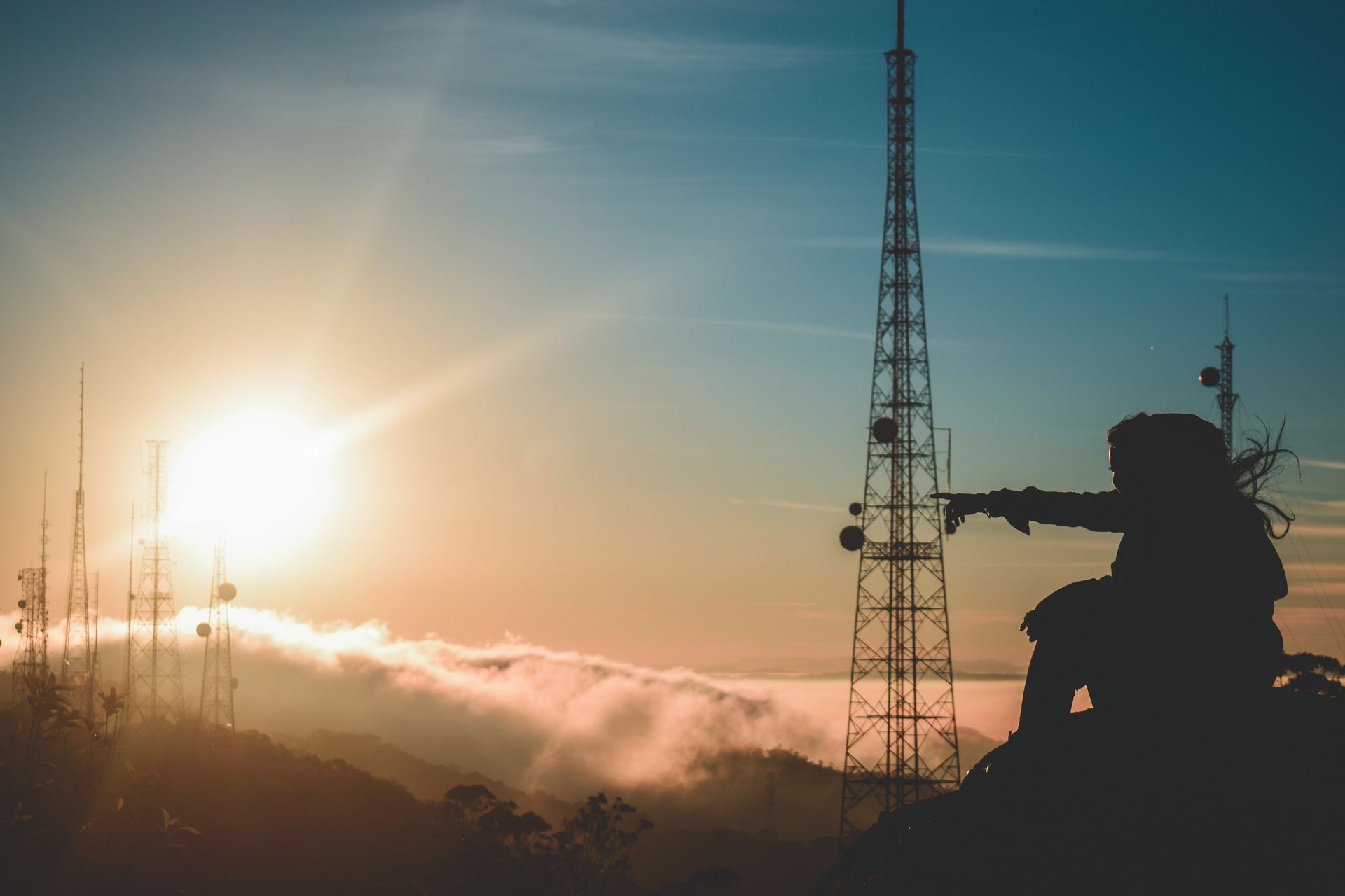 A silhouette of a man pointing against a sunset with communication towers in São Paulo.