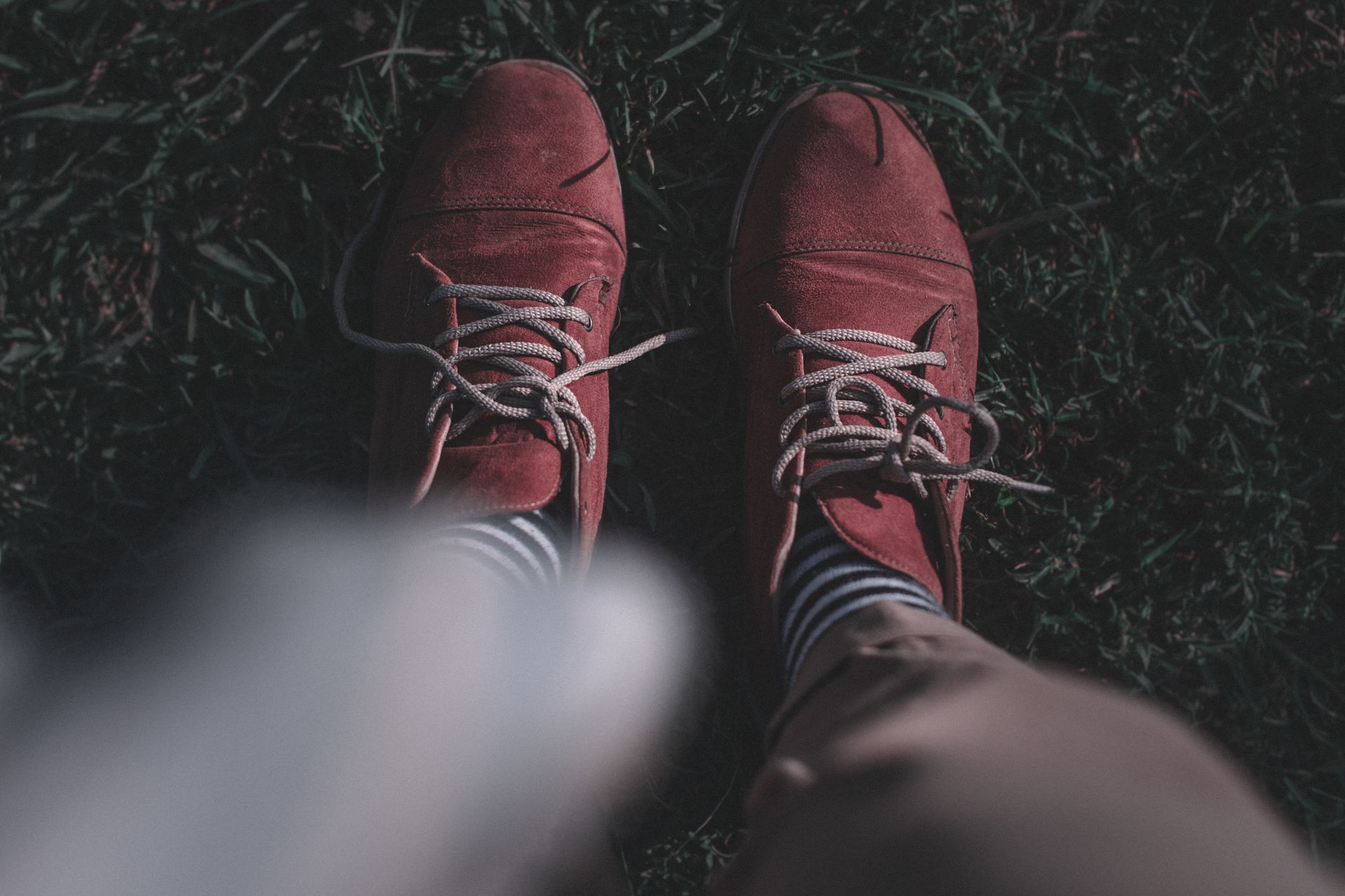Red suede shoes with striped socks in an outdoor setting, standing on grass.