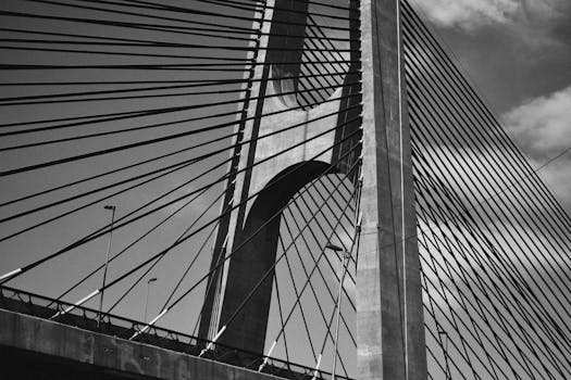 Close-up view of a suspension bridge's architectural design in black-and-white, showcasing cables and structure.