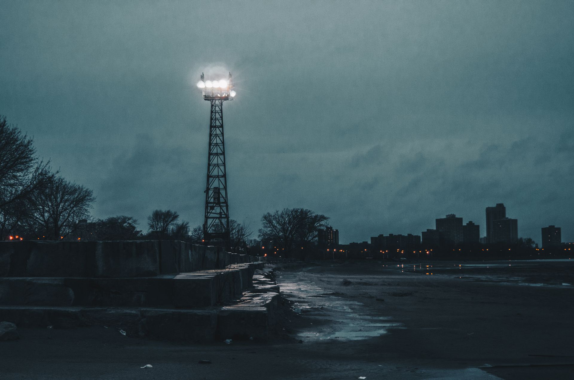 A moody dusk scene in Chicago featuring a prominent light tower illuminating the urban landscape.