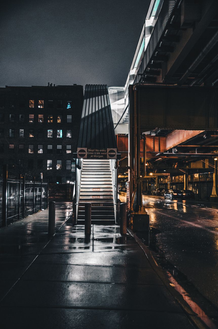 Dramatic night view of Chicago's urban architecture, highlighting a dimly lit overpass and stairs.