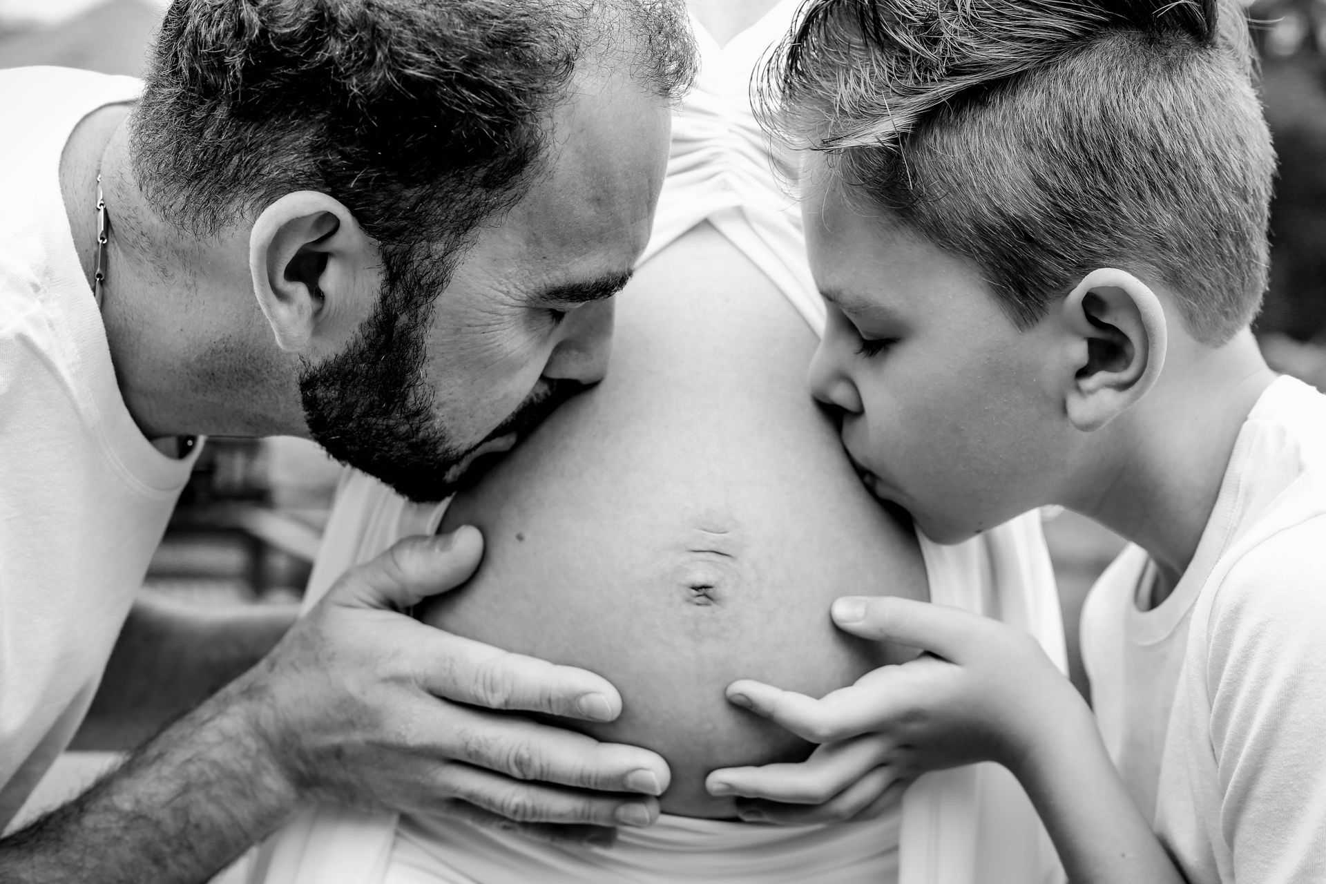 Father and son bonding with pregnant mother in an emotional black and white capture.