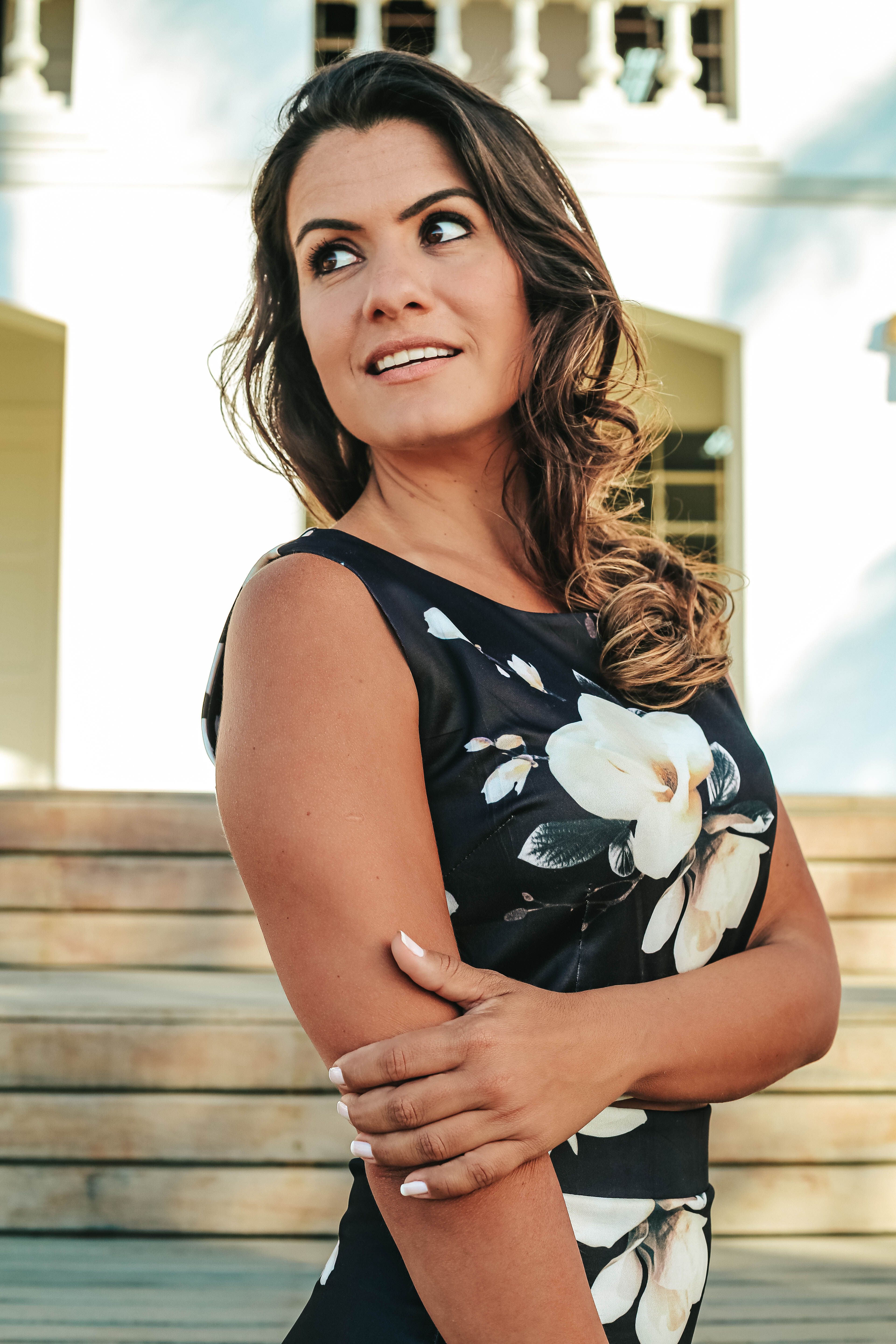 Charming woman in a floral dress poses elegantly outdoors, exuding confidence and warmth.