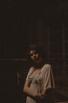 Vintage-style portrait of a woman in nightwear, captured in moody lighting with a dark background.