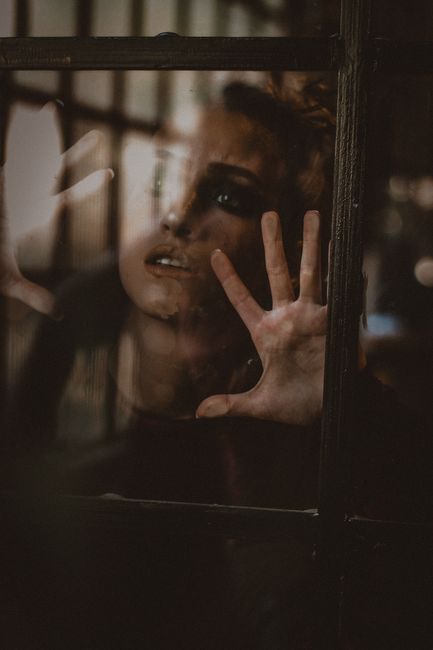 A dramatic portrait of a woman looking through a glass window with her hand pressed against it.