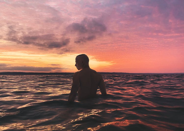 Back View Of A Man In The Sea During Pink Sky