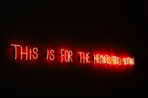 Free Red neon sign with the message 'THIS IS FOR THE HEARTS STILL BEATING' against a dark backdrop. Stock Photo