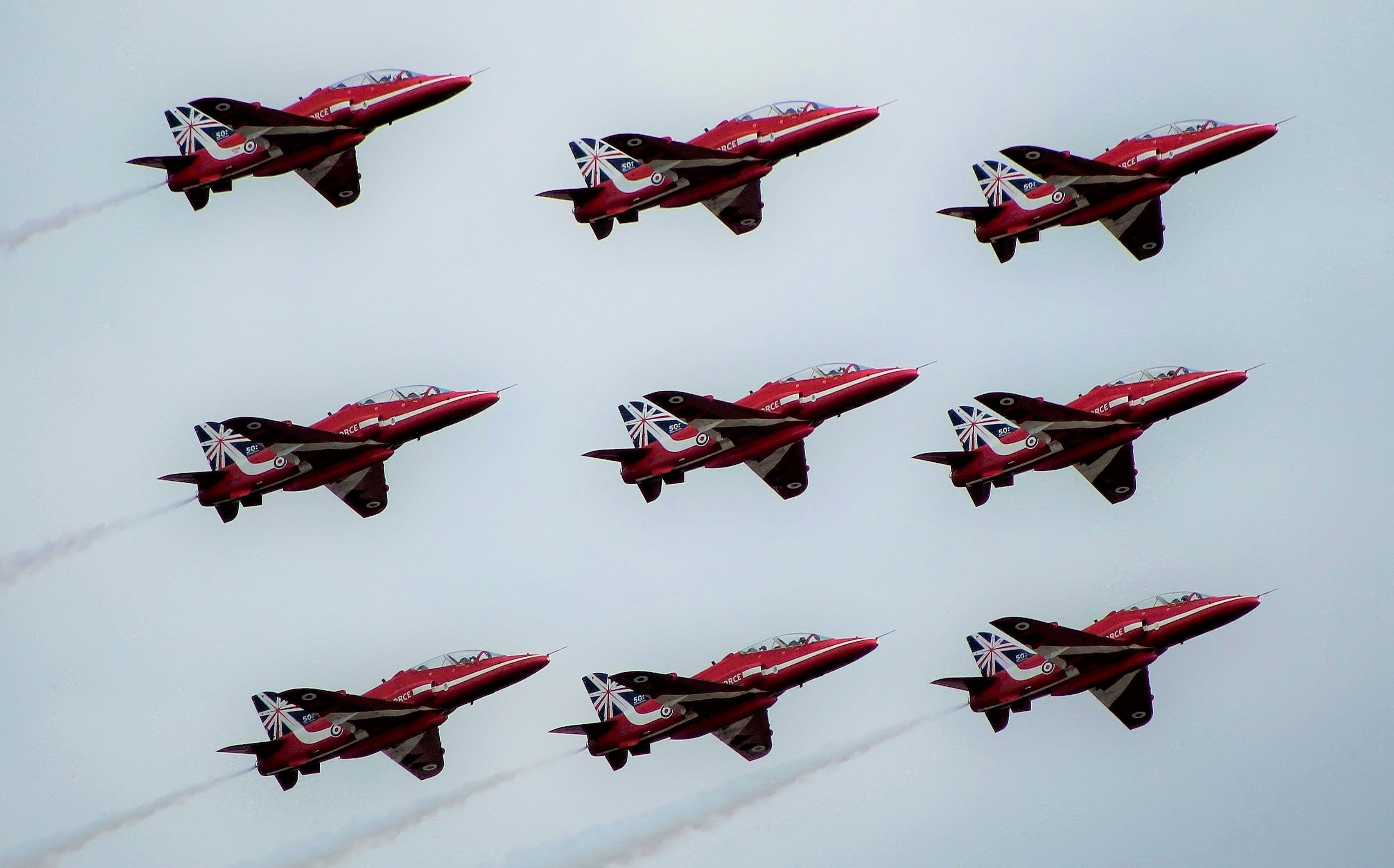 A formation of red military aircrafts performing an aerobatic display against a clear sky.