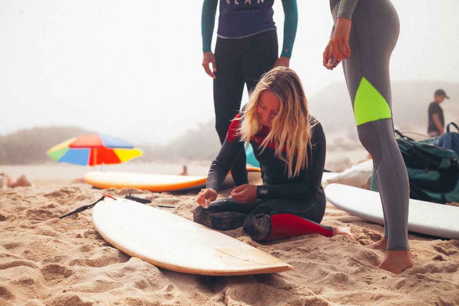 Group of surfers in wetsuits preparing surfboards on Ericeira beach, Portugal.