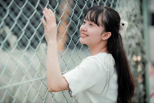 Young Woman with Black Long Hair Standing Near a Chain Link Fence