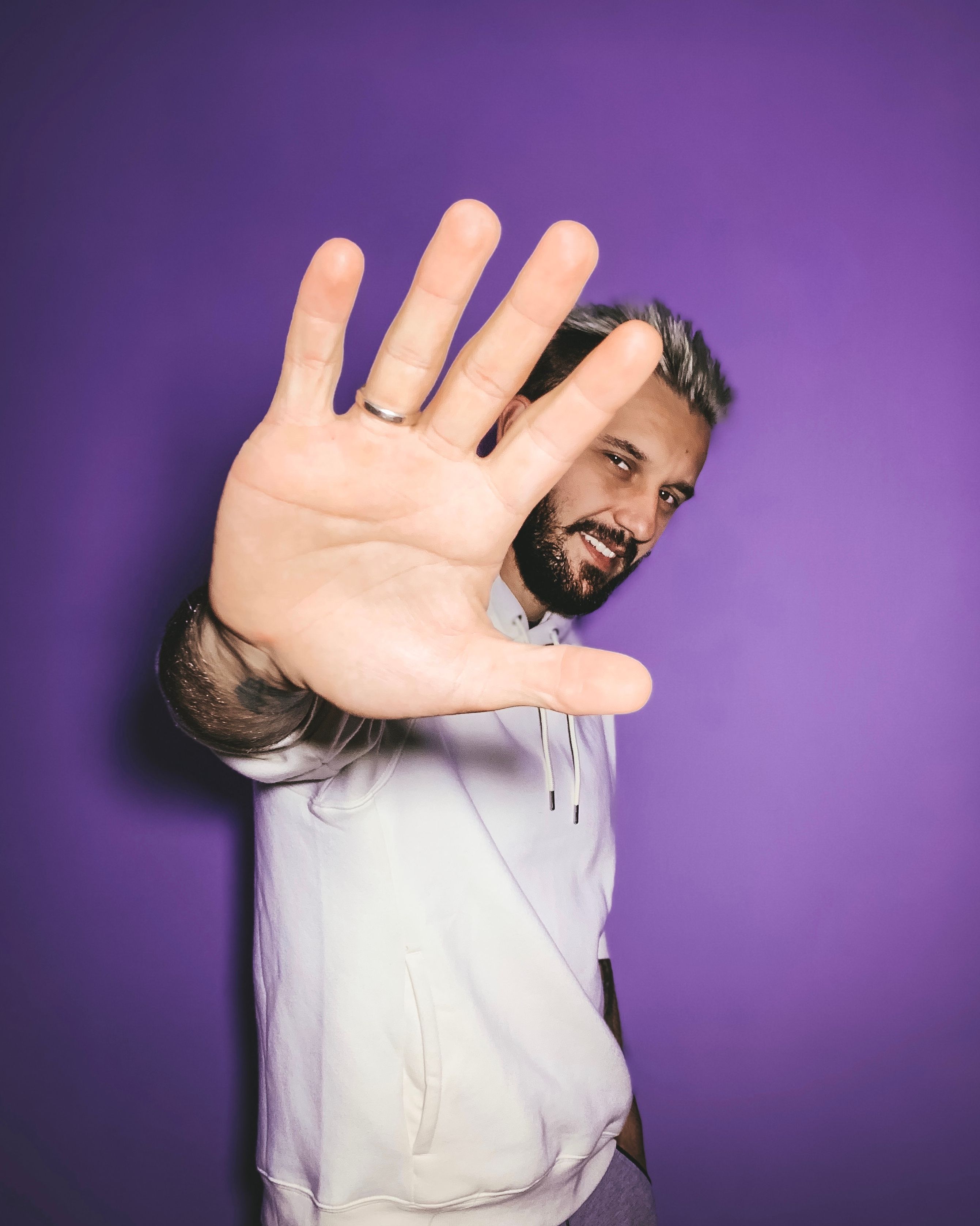 Smiling man with outstretched hand against purple background in playful pose.