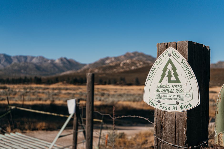 Close-up of National Forest Adventure Pass sign on wooden post with mountains in the background.