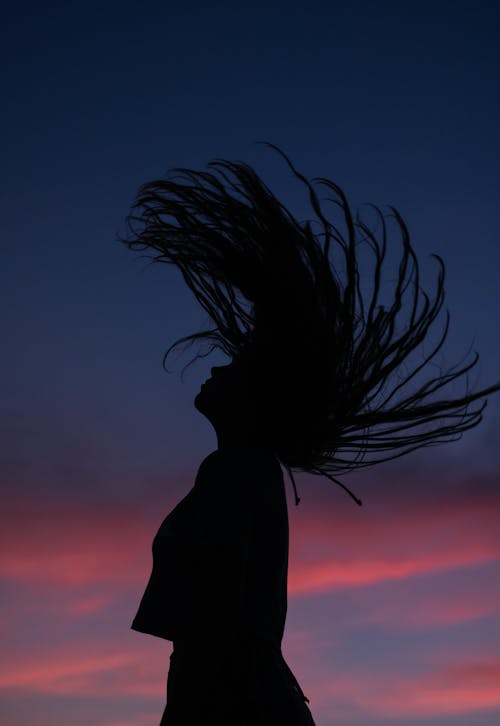 Side view silhouette of slim female raising head with flying long hair against amazing dark purple sky in evening