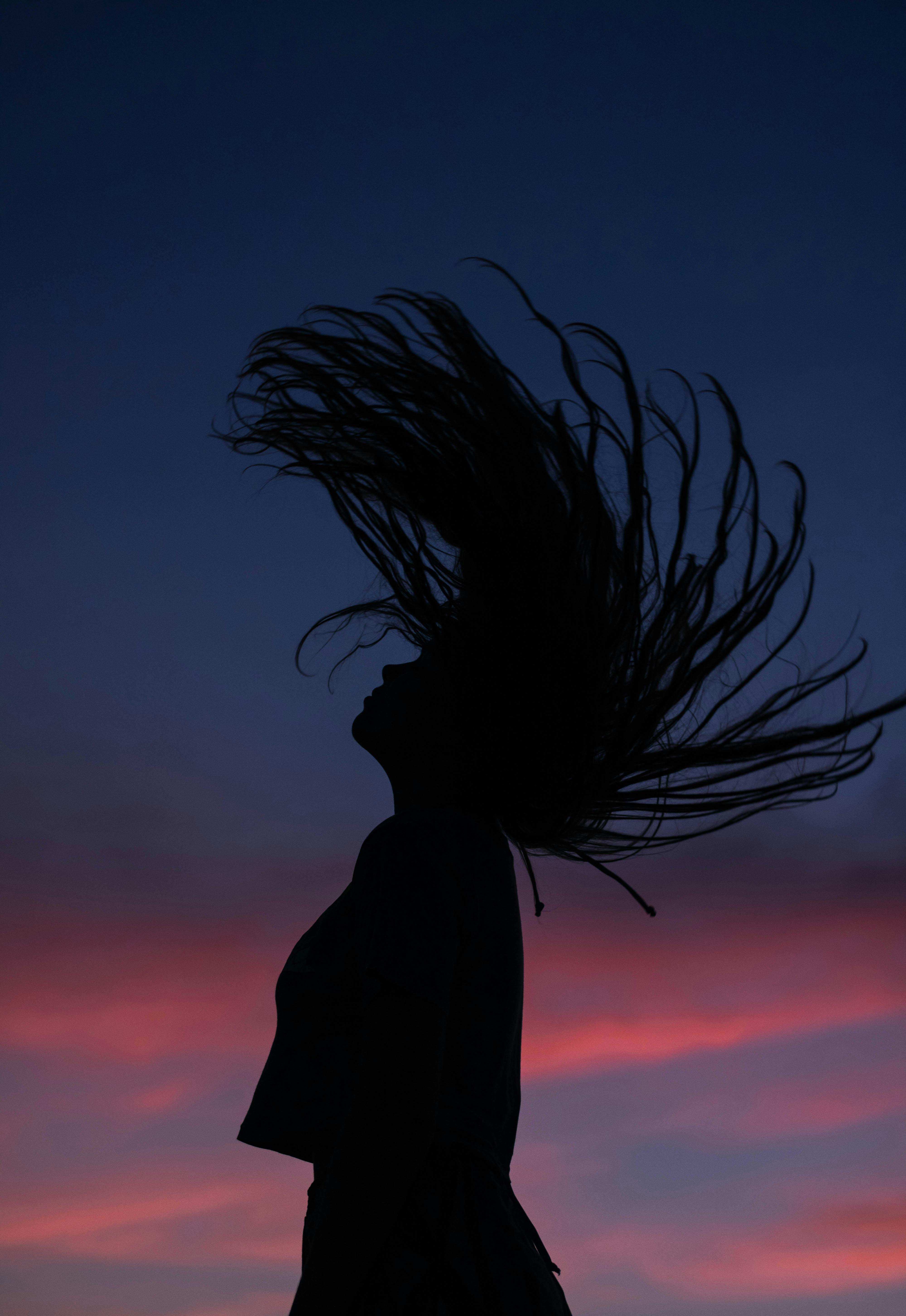 Woman silhouette shaking head with flying hair against purple sky ...