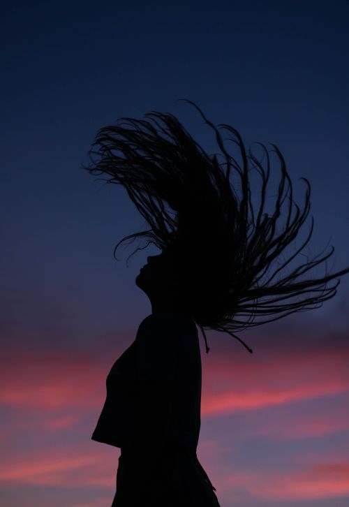 Free Side view silhouette of slim female raising head with flying long hair against amazing dark purple sky in evening Stock Photo