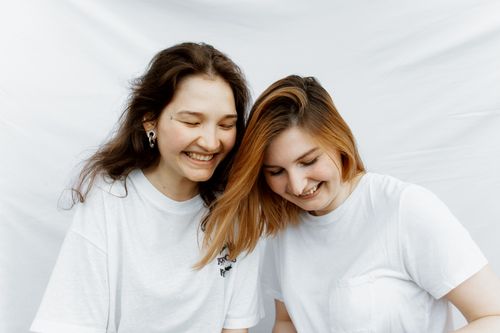 Free Two friends joyfully smiling together in a simple white setting. Stock Photo