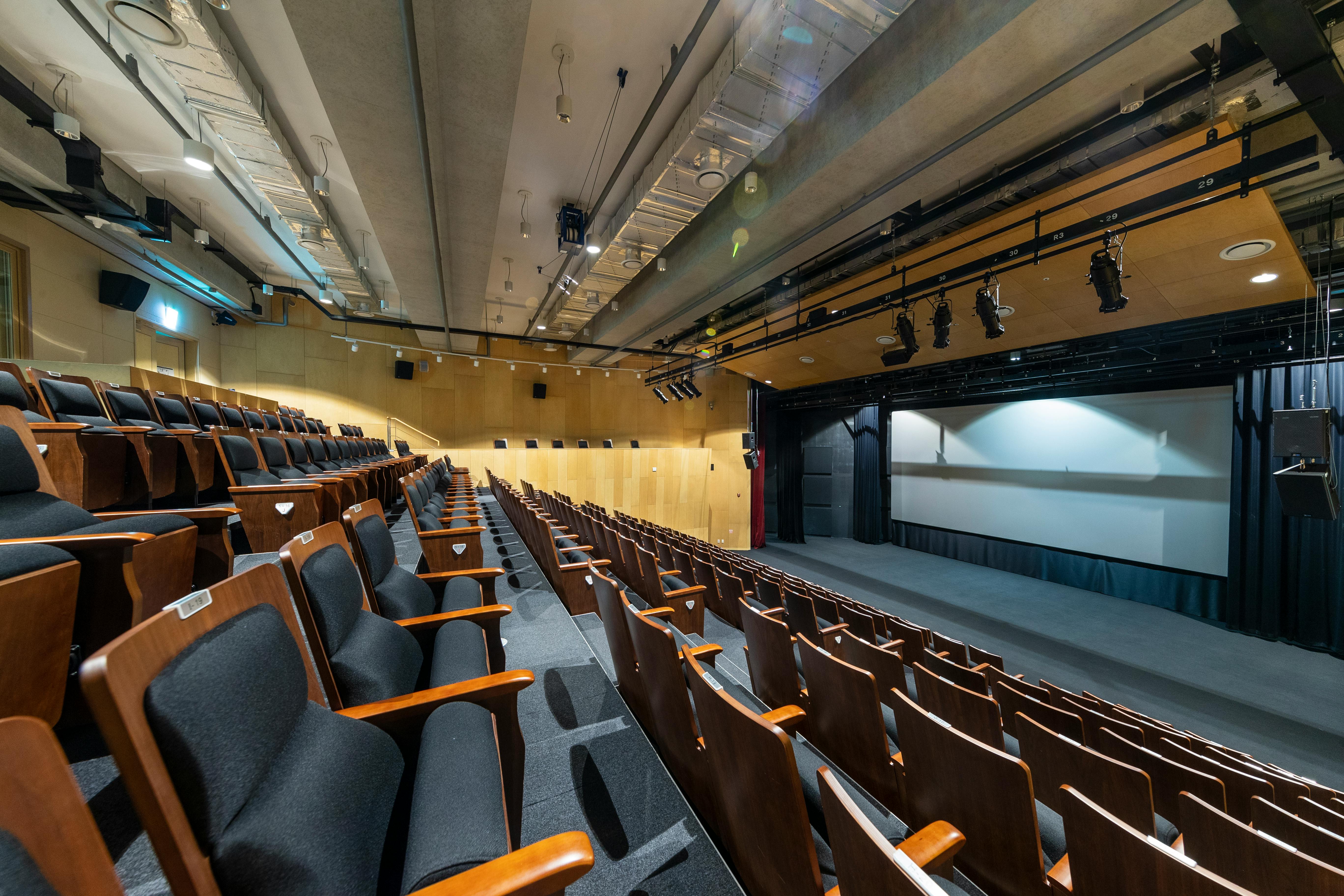 Free Spacious empty auditorium with wooden seats and projection screen in a modern setting. Stock Photo
