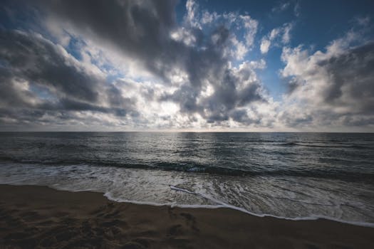 Scenic view of the ocean with dramatic clouds and gentle waves at sunset, evoking tranquility and beauty.