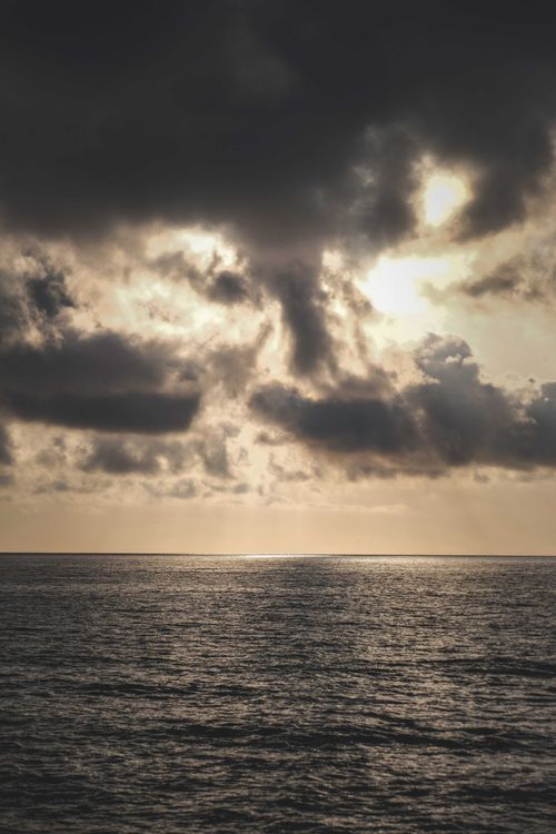 Free Picturesque view of calm ocean water under bright sundown behind dark massive clouds Stock Photo