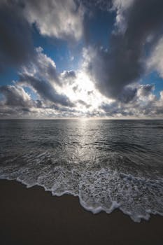 Picturesque view of foamy waves of ocean washing sandy shore under cloudy sky at sundown