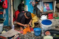 Adult man cleaning utensils outside his home in Jakarta, showcasing daily routines.