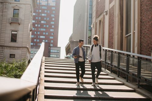 Free Full body of cheerful multiracial students in casual clothes walking downstairs among buildings in city in sunny day Stock Photo