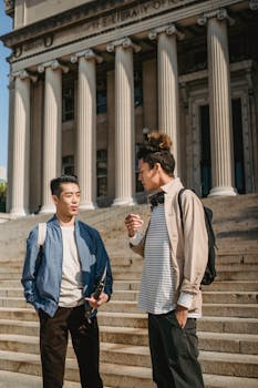 Young multiracial male students talking to each other standing together on stairs of aged university building with columns