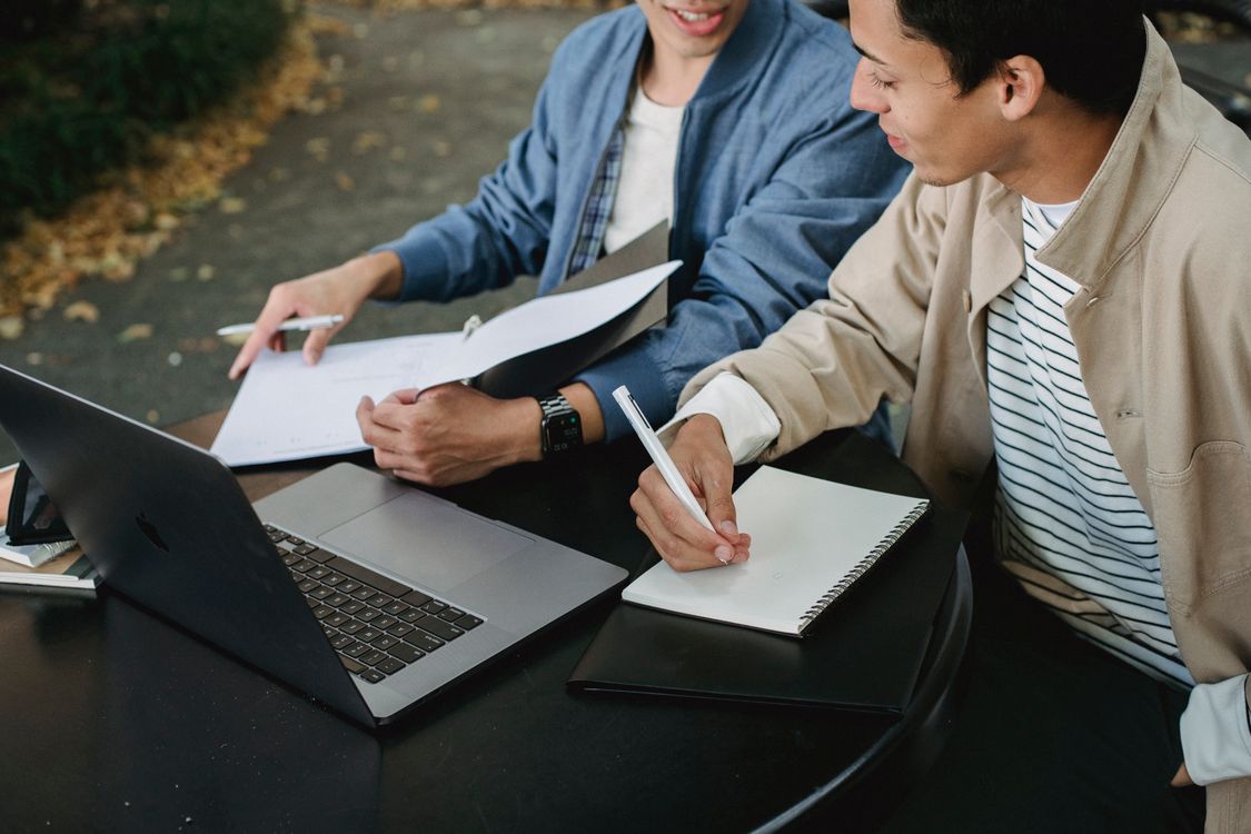 Free From above of positive male students working on laptop with documents and notebook while doing homework together Stock Photo