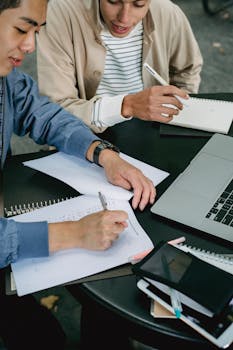 Two university students studying together with a laptop and notebooks.