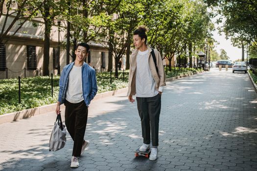 一群充满活力的年轻男性朋友，来自不同种族，穿着休闲服装，一边骑滑板一边聊天，在现代城市阳光明媚的人行道上漫步