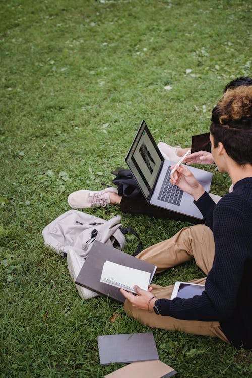 Man in Black Suit Sitting on Green Grass Field Reading Book