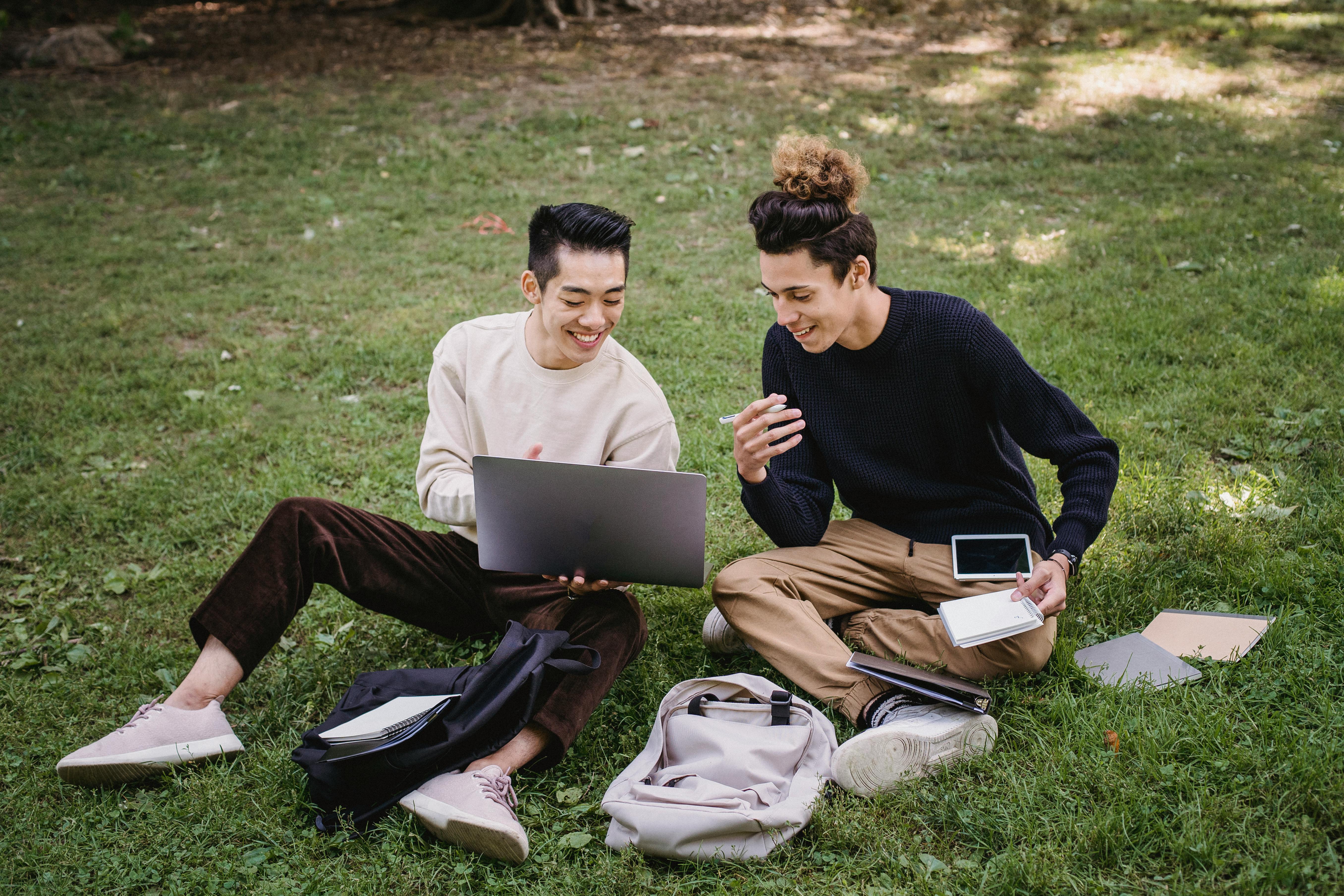 happy ethnic male students preparing for exams on park lawn