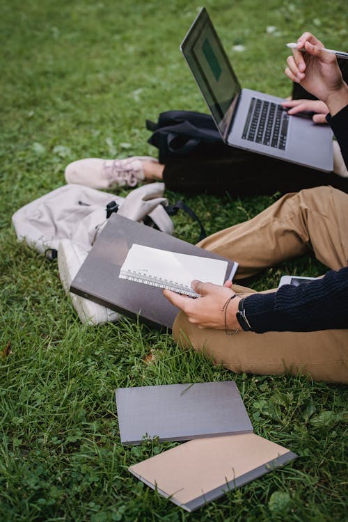 Free Crop unrecognizable students studying together on grassy meadow Stock Photo