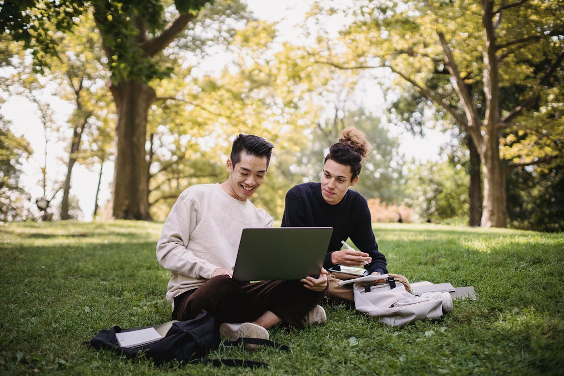 Man and Woman Sitting on Green Grass Field Using Laptop Computer