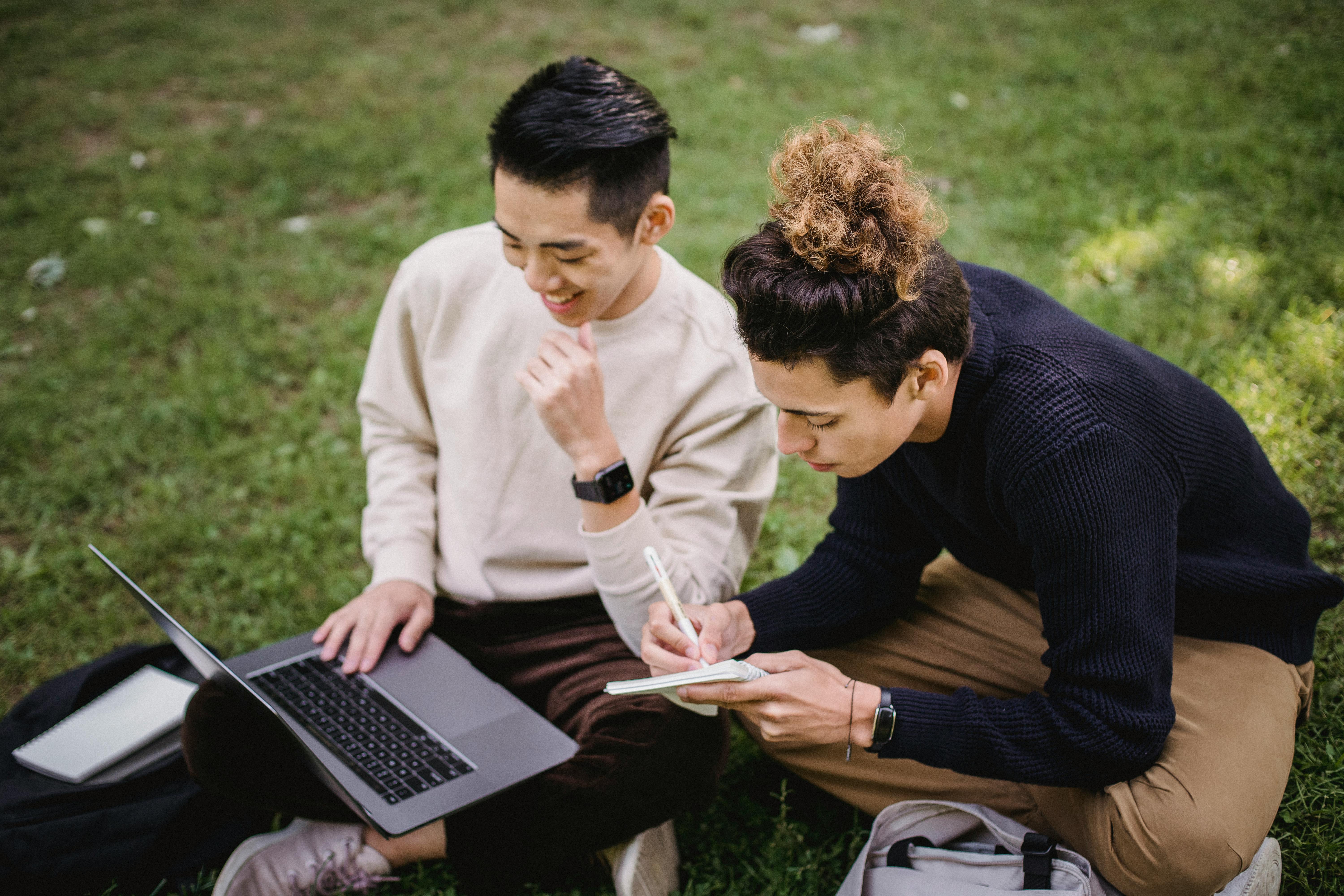 cheerful ethnic male students working on project in park