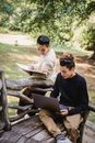 在阳光明媚的公园里，穿着休闲服装的快乐年轻少数族裔男学生们一起学习，他们浏览着现代笔记本电脑，并在笔记本上做笔记